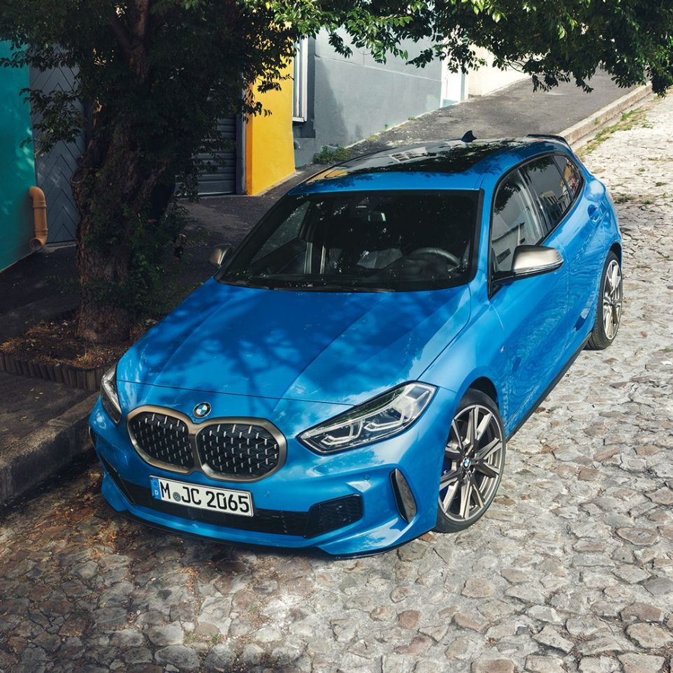 BMW řady 1 na krajnici. Tříčtvrteční pohled z ptačí perspektivy na BMW řady 1 v modré metalické barvě Misano Blue, zaparkované na krajnici.
