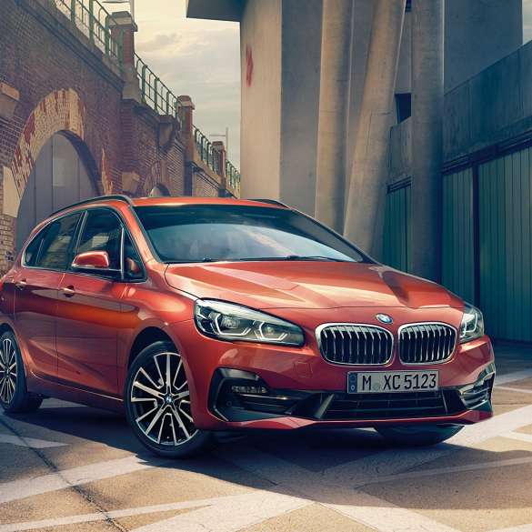 Exteriér BMW řady 2 Active Tourer BMW řady 2 Active Tourer F45 2018 v metalické barvě Sunset Orange (oranžová) ze tříčtvrtečního pohledu zepředu zaparkované na ulici