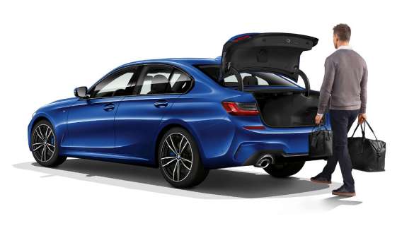 BMW řady 3 Sedan, automatické víko zavazadlového prostoru Zadní tříčtvrteční pohled na stojící BMW řady 3 Sedan s řidičem, který nohou otevírá automatické víko zavazadelníku.