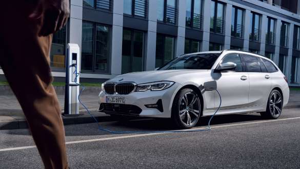Plug-in hybridní BMW řady 3 Touring 2021 G21 tříčtvrteční pohled zepředu při nabíjení Plug-in hybridní BMW řady 3 Touring 2021 G21 tříčtvrteční pohled zepředu při nabíjení před budovou