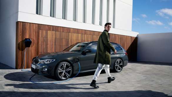 Plug-in hybridní BMW řady 3 Touring 2021 G21 z tříčtvrtečního pohledu z boku u nabíječky BMW Wallbox Plug-in hybridní BMW řady 3 Touring 2021 G21 z tříčtvrtečního pohledu z boku u nabíječky BMW Wallbox s modelem