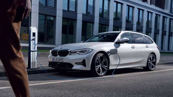 Plug-in hybridní BMW řady 3 Touring 2021 G21 ze tříčtvrtečního pohledu zepředu při nabíjení Plug-in hybridní BMW řady 3 Touring 2021 G21 ze tříčtvrtečního pohledu zepředu při nabíjení před budovou