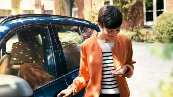 Žena se na chytrý telefon Žena vystupuje z BMW a dívá se na chytrý telefon