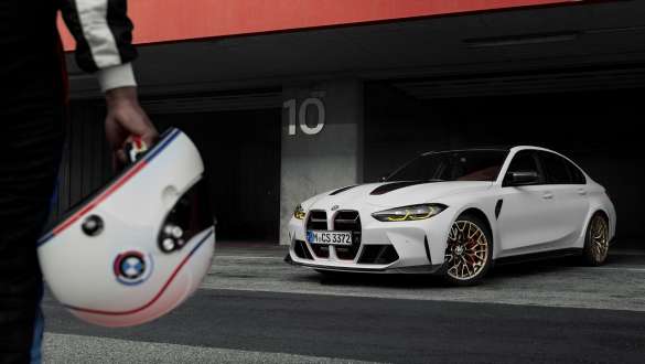 CS specifický paket Driving Dynamics BMW M3 CS G80 BMW M3 CS G80 CS specifický paket Driving Dynamics Osoba s BMW přilbou v ruce a BMW M3 CS stojícím v pozadí