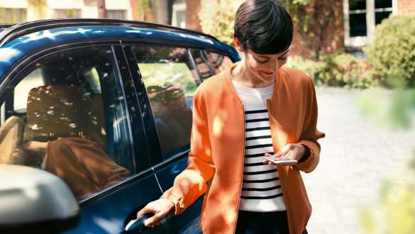 Žena hledí do displeje chytrého telefonu a otevírá dveře svého BMW BMW Teleservices žena hledí do displeje chytrého telefonu a otevírá dveře svého BMW
