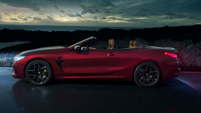 BMW M8 Competition Cabrio, pohled z boku. BMW M8 Copmpetition Cabrio v červené metalíze Motegi Red se staženou střechou, pohled z boku, stojící pod hvězdnou oblohou.
