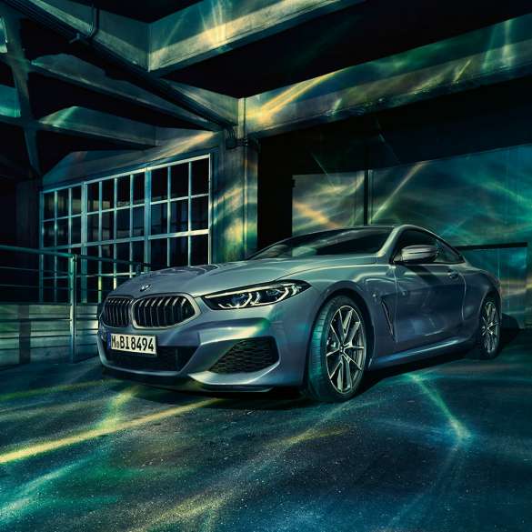 BMW M850i xDrive Coupé, tříčtvrteční pohled zpředu. BMW M850i xDrive Coupé v metalické barvě Barcelona Blue, tříčtvrteční pohled zpředu, stojící před budovou.