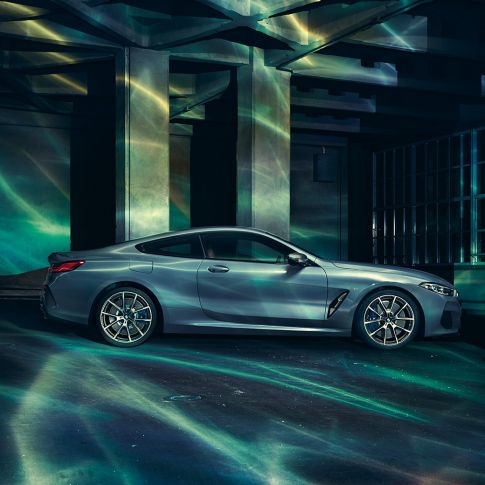 BMW M850i xDrive Coupé, boční pohled. BMW M850i xDrive Coupé v metalické barvě Barcelona Blue, stojící před budovou.