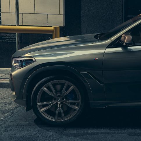 BMW X6 M50i z bočního pohledu Můž opírající se o BMW X6 M50i z bočního pohledu před městským prostředím.
