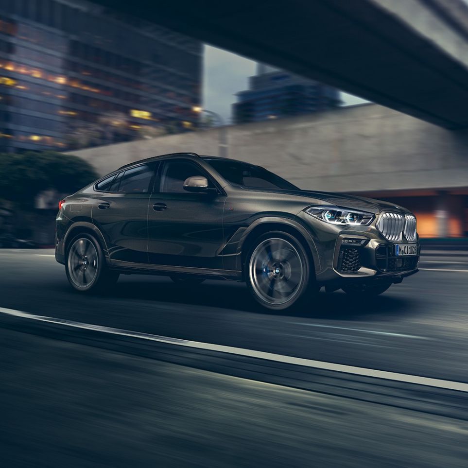 Jedoucí BMW X6. Tříčtvrteční pohled na BMW X6 před městským prostředím.