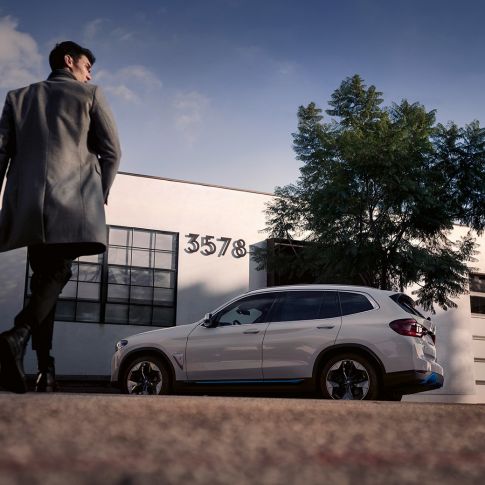 BMW iX3 G08 boční pohled před budovou s mužem BMW iX3 G08 2020 v metalické barvě Mineral White (bílá) boční pohled před budovou s mužem