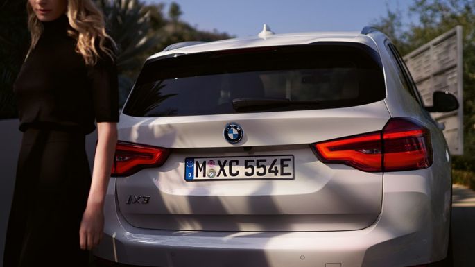 Záď se specifickým BMW i difuzorem BMW iX3 G08 2020, pohled zezadu, s ženou Záď se specifickým BMW i difuzorem BMW iX3 G08 2020 v metalické barvě Mineral White (bílá), pohled zezadu, s ženou