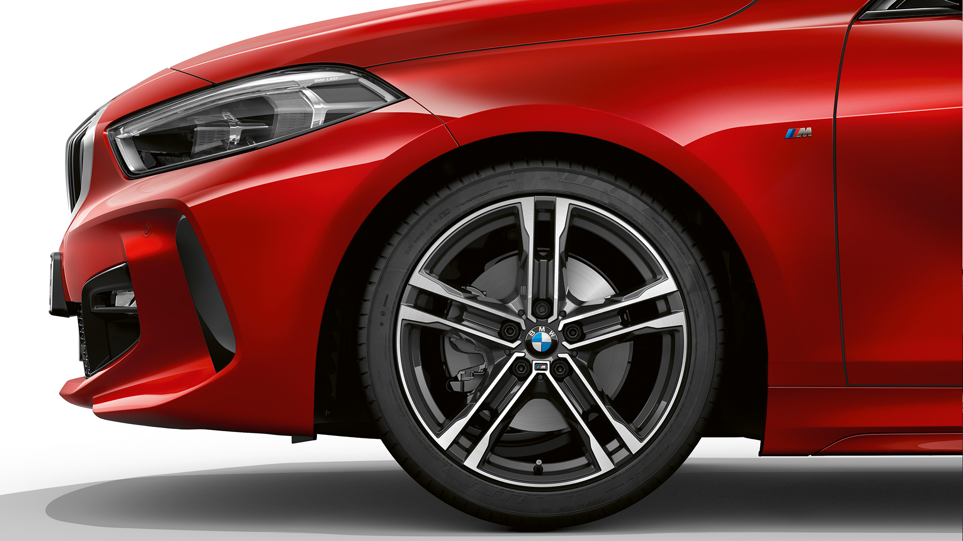 BMW řady 1 Model M Sport, boční pohled na přední část. BMW řady 1 Model M Sport v červené metalické barvě Melbourne Red, boční pohled na přední část se 17" M koly z lehké slitiny Double-spoke 550 M Bicolour.