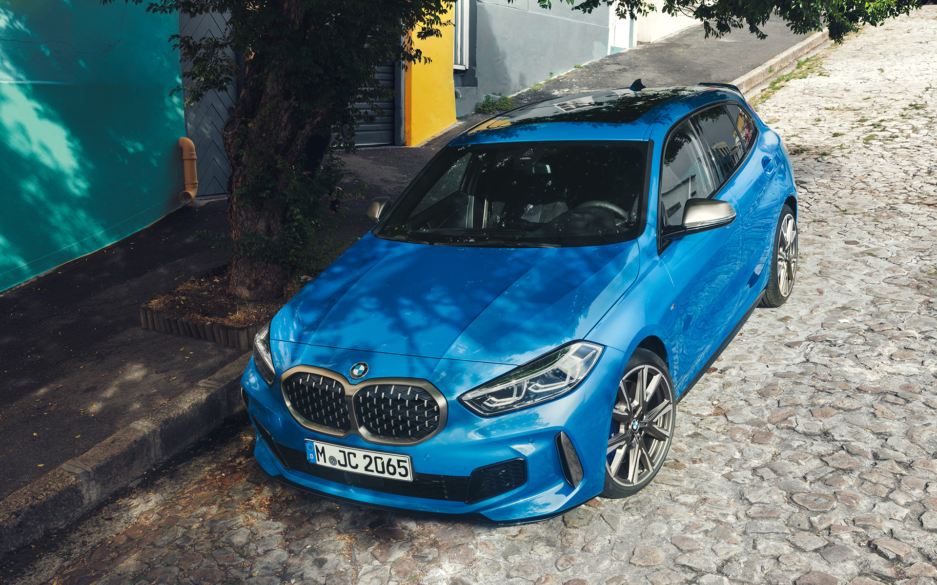 BMW řady 1 M135i F40 vedle silnice BMW řady 1 M135i F40 v metalickém laku Misano Blue (modrá), ze tříčtvrtečního pohledu zepředu parkuje vedle silnice z ptačího pohledu