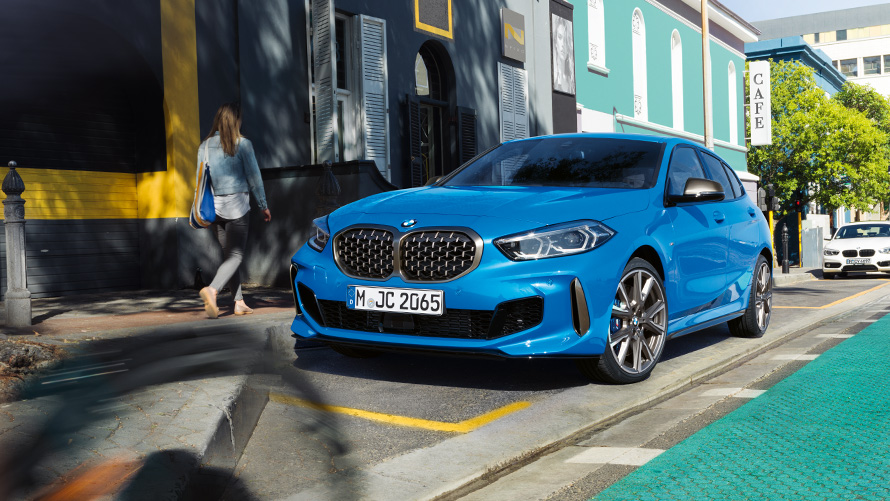 BMW řady 1 F40 metalický lak Misano Blue (modrá), tříčtvrteční záběr zepředu BMW řady 1 F40 metalický lak Misano Blue (modrá), tříčtvrteční záběr zepředu parkující u silnice ze ženou