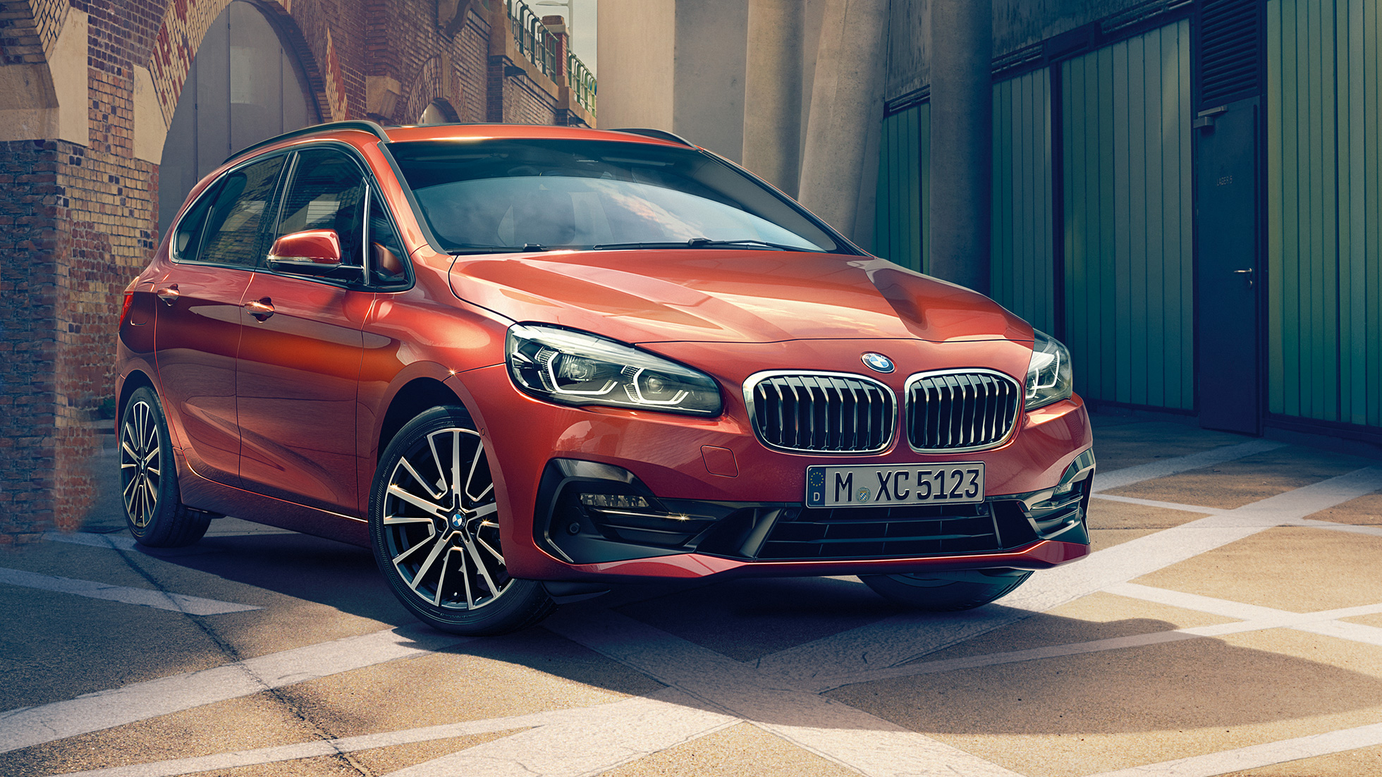 Exteriér BMW řady 2 Active Tourer BMW řady 2 Active Tourer F45 2018 v metalické barvě Sunset Orange (oranžová) ze tříčtvrtečního pohledu zepředu zaparkované na ulici