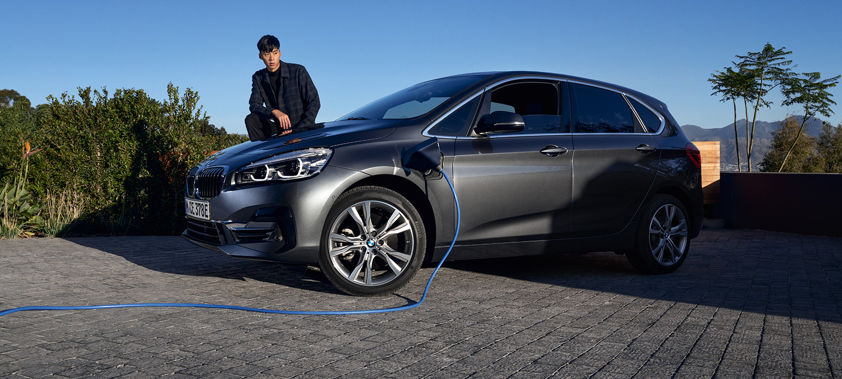 Plug-in hybridní BMW 225xe Active Tourer F45 tříčtvrteční pohled z boku u nabíjecí stanice Plug-in hybridní BMW 225xe Active Tourer F45 tříčtvrteční pohled z boku u nabíjecí stanice s modelem