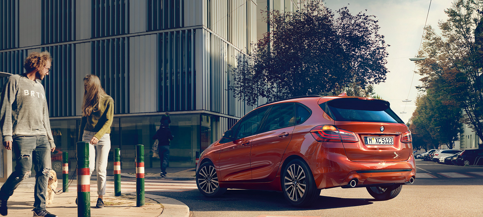 Tříčtvrteční pohled zezadu BMW řady 2 Active Tourer 220i BMW řady 2 Active Tourer 220i F45 v metalické barvě Sunset Orange (oranžová) ze tříčtvrtečního pohledu zezadu při jízdě po ulici