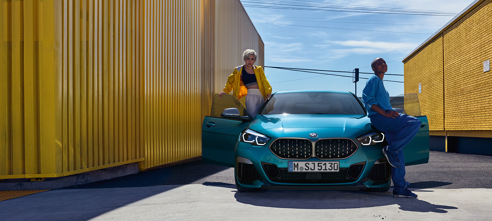 BMW řady 2 Gran Coupé F44, pohled zepředu BMW řady 2 Gran Coupé F44 Snapper Rocks Blue (modrá), pohled zepředu s otevřenými dveřmi a dvěma osobami u vozidla