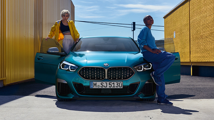 BMW řady 2 Gran Coupé F44, pohled zepředu BMW řady 2 Gran Coupé F44 Snapper Rocks Blue (modrá), pohled zepředu s otevřenými dveřmi a dvěma osobami u vozidla