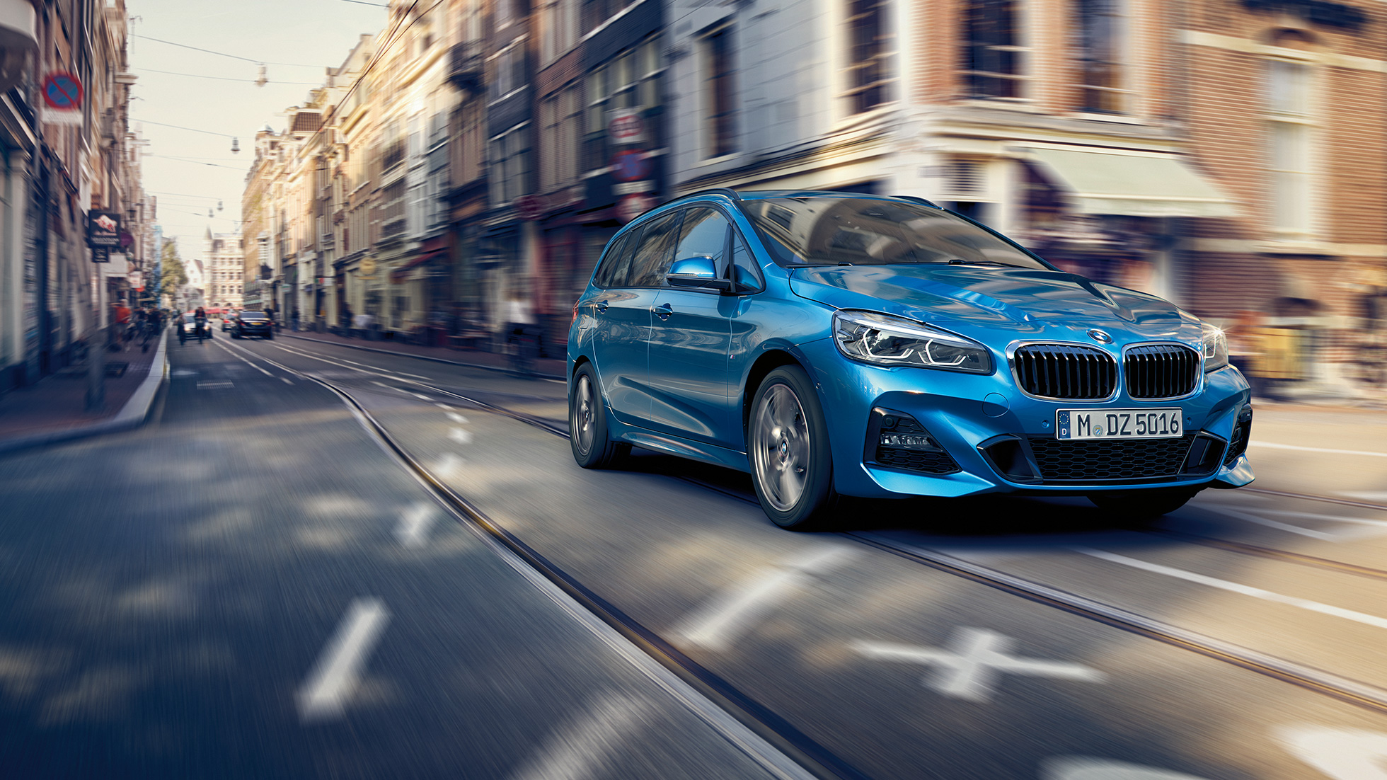 Jízdní dynamika BMW řady 2 Gran Tourer Jízdní dynamika BMW řady 2 Gran Tourer F46 2018 v metalické barvě Misano Blue (modrá) ze tříčtvrtečního pohledu zezadu při jízdě centrem města
