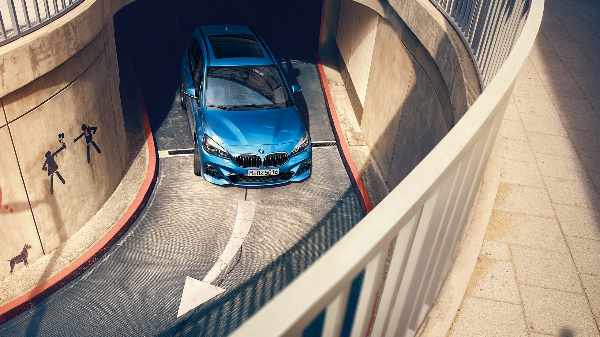 BMW řady 2 Gran Tourer při jízdě parkovacím domem BMW řady 2 Gran Tourer F46 v metalické 2018 barvě Misano Blue (modrá) pohled z ptačí perspektivy při jízdě parkovacím domem