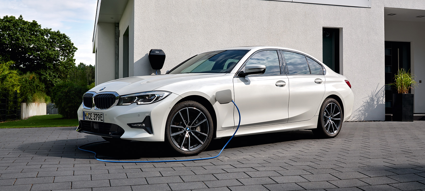 Plug-in hybridní BMW řady 3 Sedan 2021 G20 tříčtvrteční pohled z boku při nabíjení Plug-in hybridní BMW řady 3 Sedan 2021 G20 tříčtvrteční pohled z boku při nabíjení před garáží