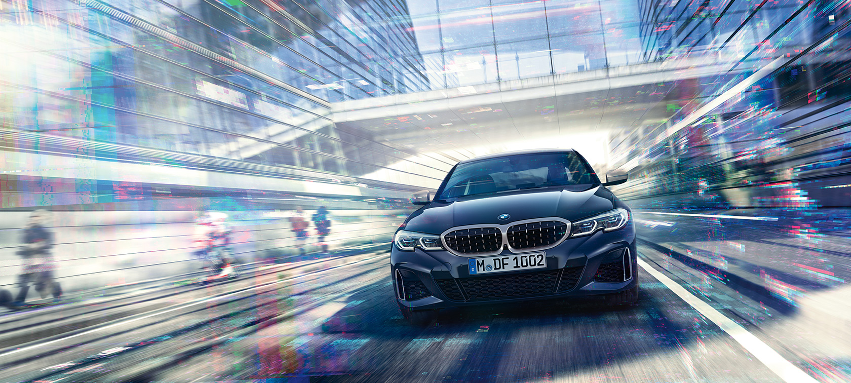 BMW řady 3 Sedan, přední pohled na BMW M340i xDrive. Přední pohled na BMW M340i xDrive Sedan v jízdě mezi skleněnými budovami.