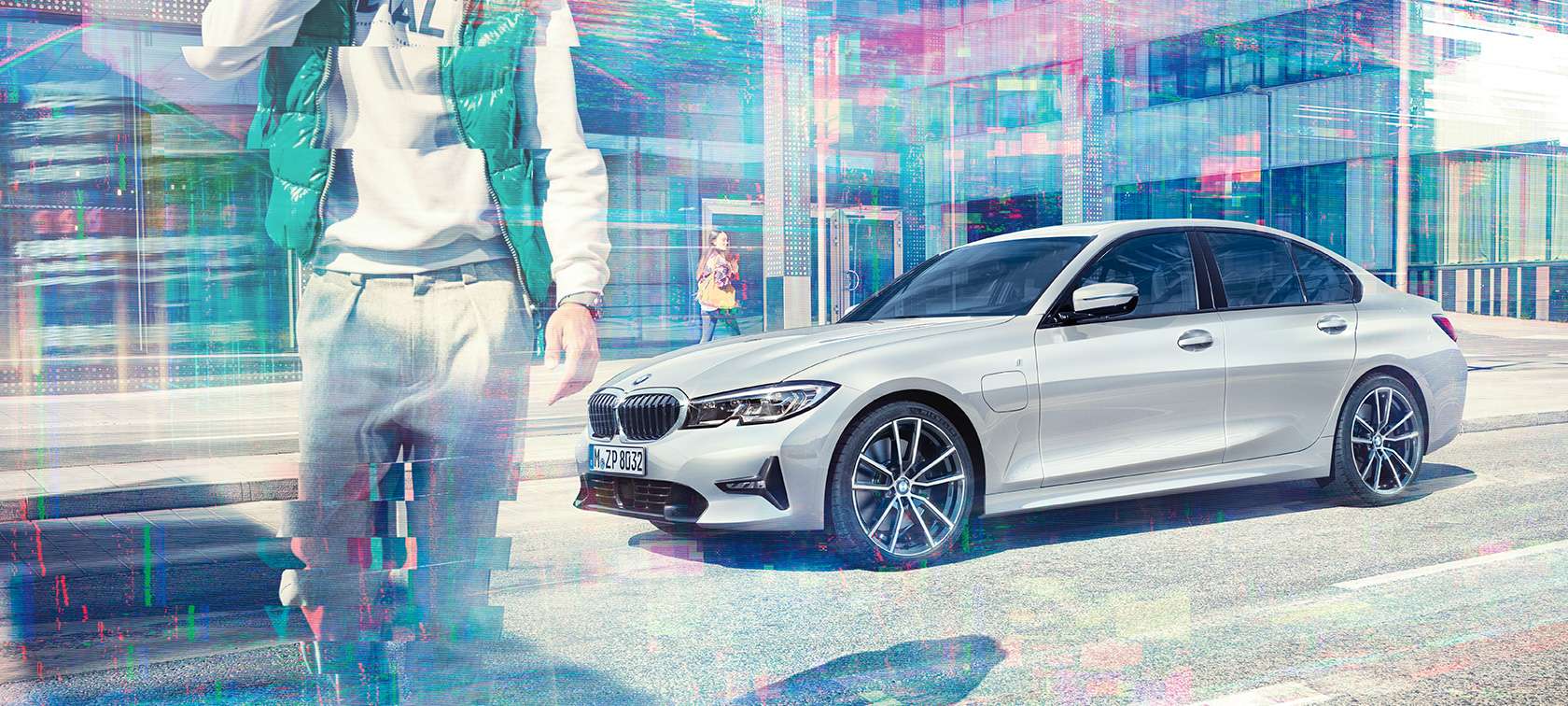 BMW řady 3 Sedan, boční pohled na BMW 330e. Tříčtvrteční pohled z boku na stojící BMW 330e před prosklenými městskými budovami s chodci.