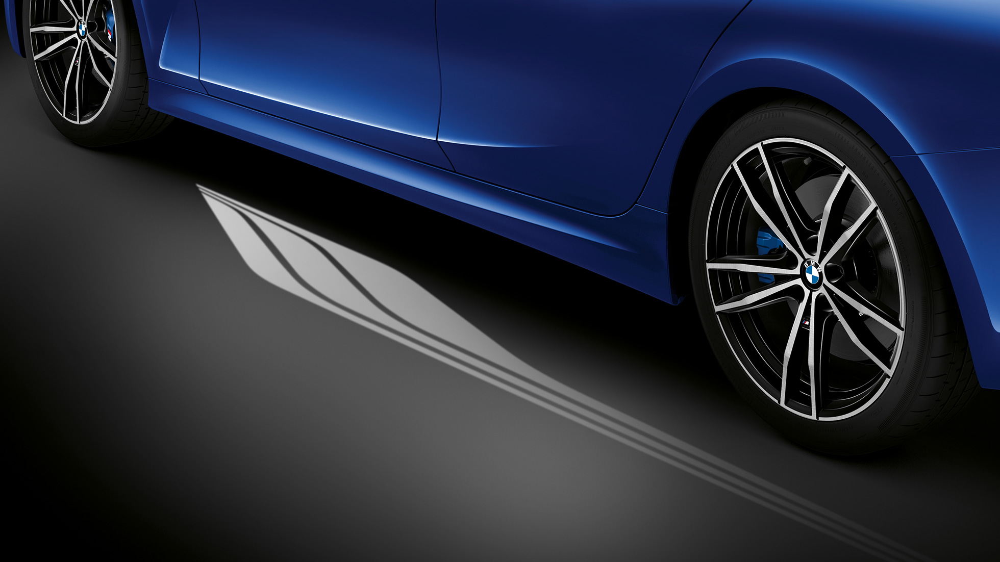 BMW řady 3 Sedan, Světelný koberec. Detail ze strany do interiéru otevřenými dveřmi řidiče se světelným kobercem rozsvíceným vedle vozu.