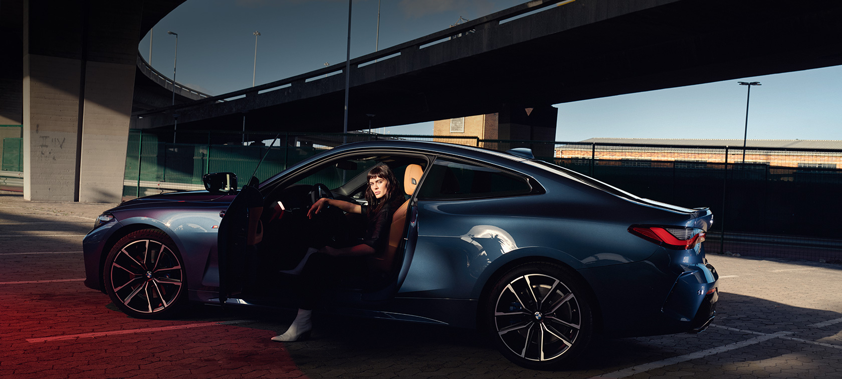 Tříčtvrteční pohled zezadu BMW řady 4 Coupé G22 2020 BMW řady 4 Coupé G22 2020 v metalické barvě Arctic Race Blue (modrá) ze tříčtvrtečního pohledu zezadu zadní světlomety s modelem stojícím vedle vozu