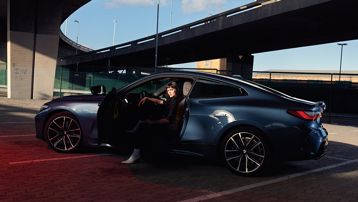 Boční pohled kola z lehké slitiny BMW řady 4 Coupé G22 2020 BMW řady 4 Coupé G22 2020 v metalické barvě Arctic Race Blue (modrá) z bočního pohledu s detailem na kolo model ve voze s otevřenými dveřmi
