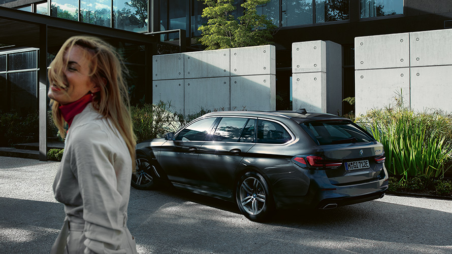Žena BMW řady 5 Touring G31 LCI Sophisto Grey (šedá), 7/8 záběr z boku Žena před parkujícím BMW řady 5 Touring G31 Facelift 2020 Sophisto Grey (šedá), 7/8 záběr z boku