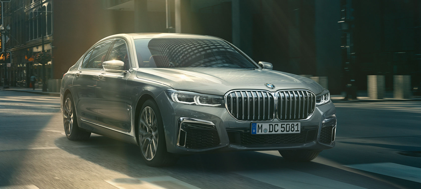 Jedoucí šedé BMW řady 7 Sedan, tříčtvrteční přední pohled Tříčtvrteční přední pohled na šedé BMW řady 7 Sedan projíždějící městským prostředím