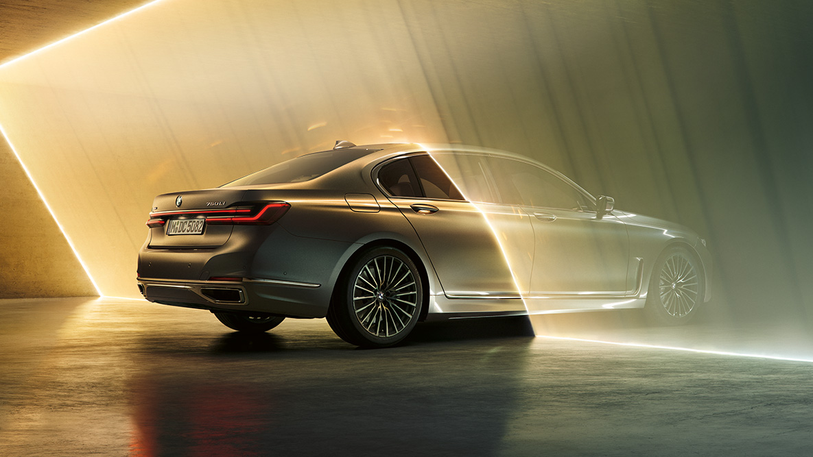 BMW řady 7 Sedan v šedé Bernina Grey Zadní tříčtvrteční pohled na BMW řady 7 Sedan v šedé Bernina Grey, obklopené paprsky světla