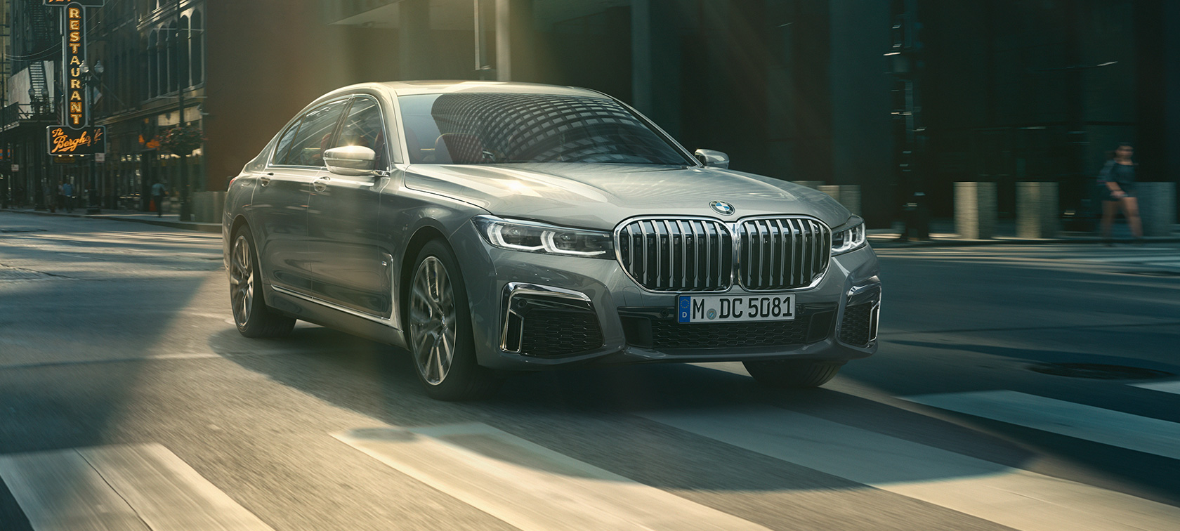 Šedé jedoucí BMW řady 7 Sedan, tříčtvrteční pohled zepředu Šedé BMW řady 7 Sedan jede městem ze tříčtvrtečního pohledu zepředu