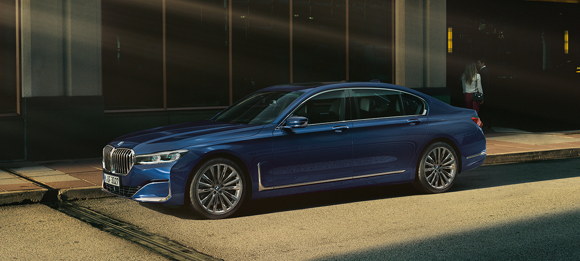 BMW Individual řady 7 Sedan z boku před městským pozadím BMW Individual řady 7 Sedan v červené barvě z boku před městským pozadím