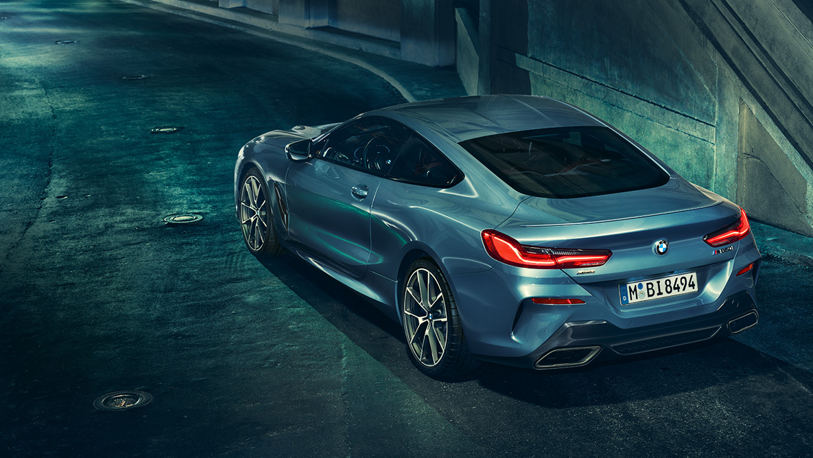 BMW řady 8 Coupé, tříčtvrteční pohled zezadu. Tříčtvrteční pohled zezadu na BMW řady 8 Coupé v noci před městskou zástavbou.