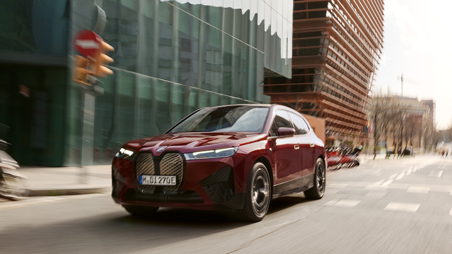 BMW iX i20 elektrické SUV BMW iX xDrive50 asistenční systémy BMW iX i20 2021 elektrické SUV BMW iX xDrive50 Aventurin Red (červená) jedoucí po městě