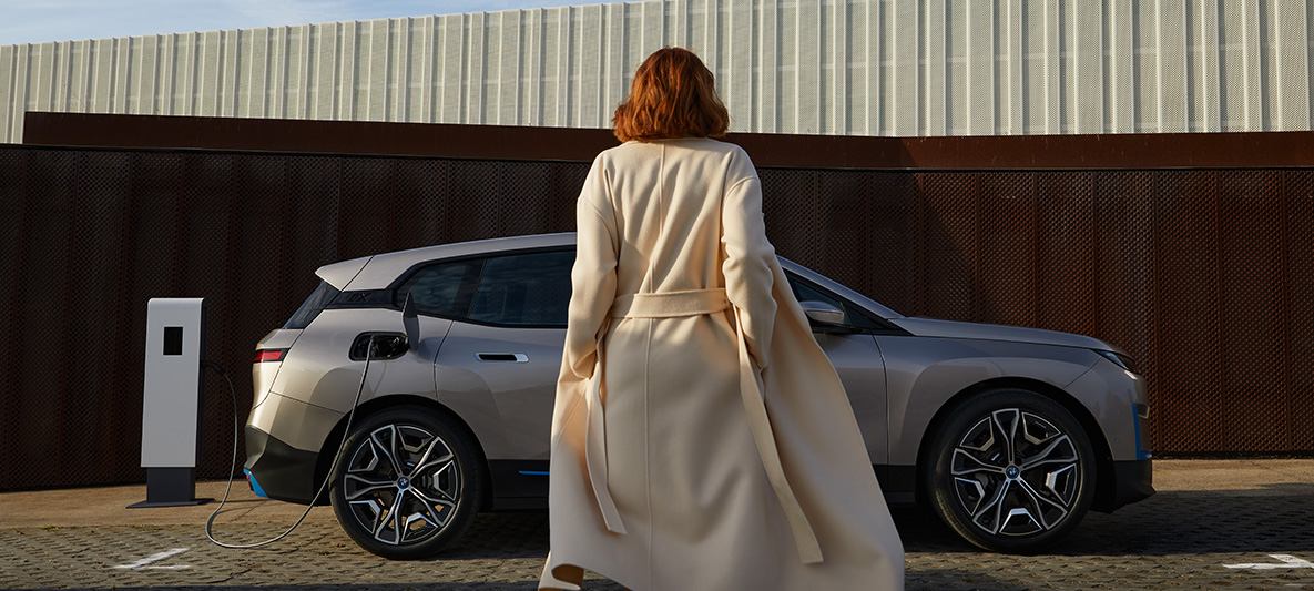 BMW iX pohled z boku s modelem stojícím vpředu BMW iX Cashmere Silver i20 pohled z boku s modelem stojícím vpředu