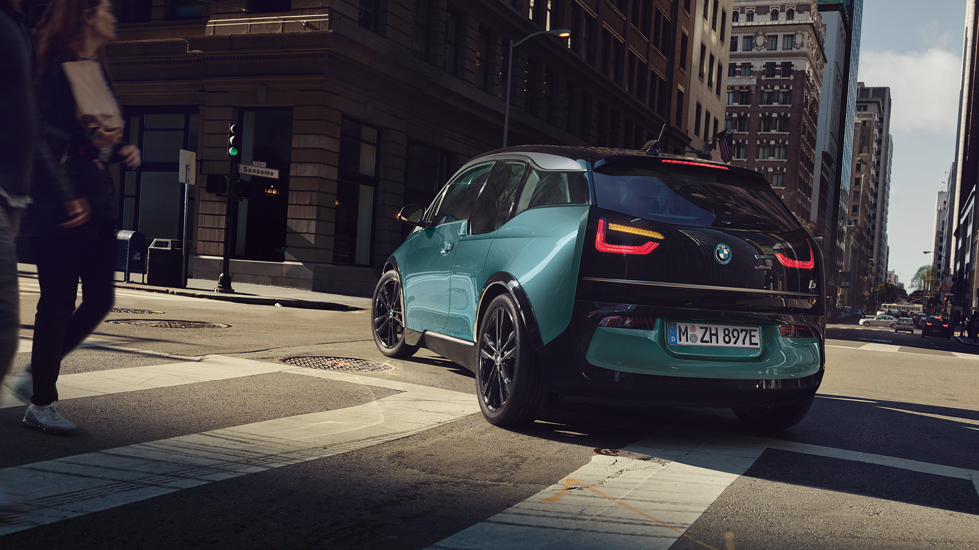 BMW i3 2018 ze tříčtvrtečního pohledu zezadu při jízdě BMW i3 I01 2018 v barvě Jucaro (béžová) s matně šedými kontrastními prvky Frozen Grey ze tříčtvrtečního pohledu zezadu ve městě