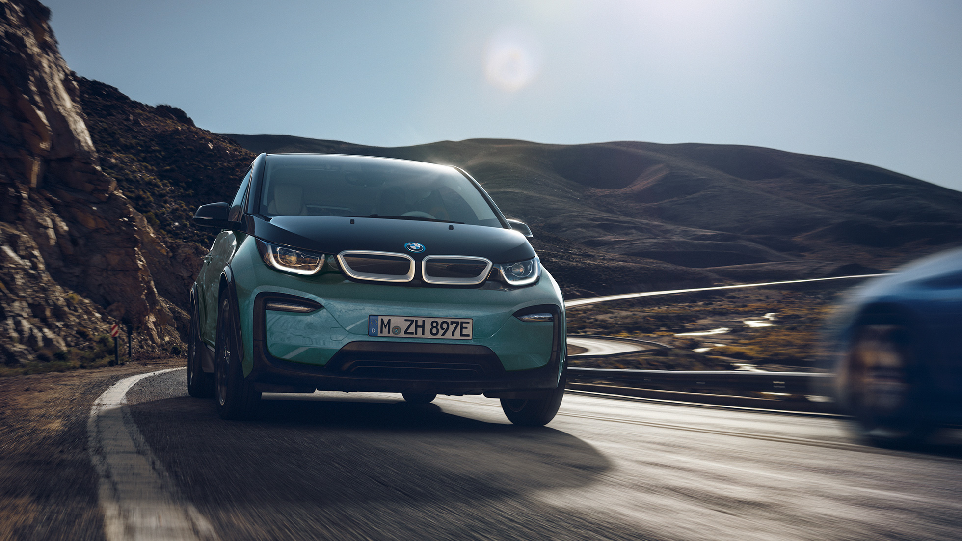 BMW i3 2018 při jízdě zboku BMW i3 I01 2018 v barvě Jucaro (béžová) s matně šedými kontrastními prvky Frozen Grey při jízdě z boku ve městě