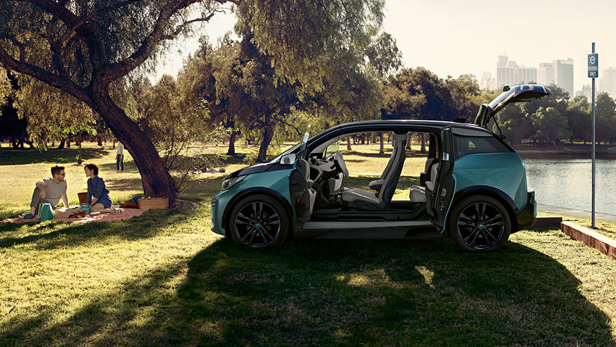 BMW i3 2018 v parku BMW i3 I01 2018 v béžové barvě Jucaro s matně šedými kontrastními prvky Frozen Grey z bočního pohledu s otevřenými dveřmi v parku