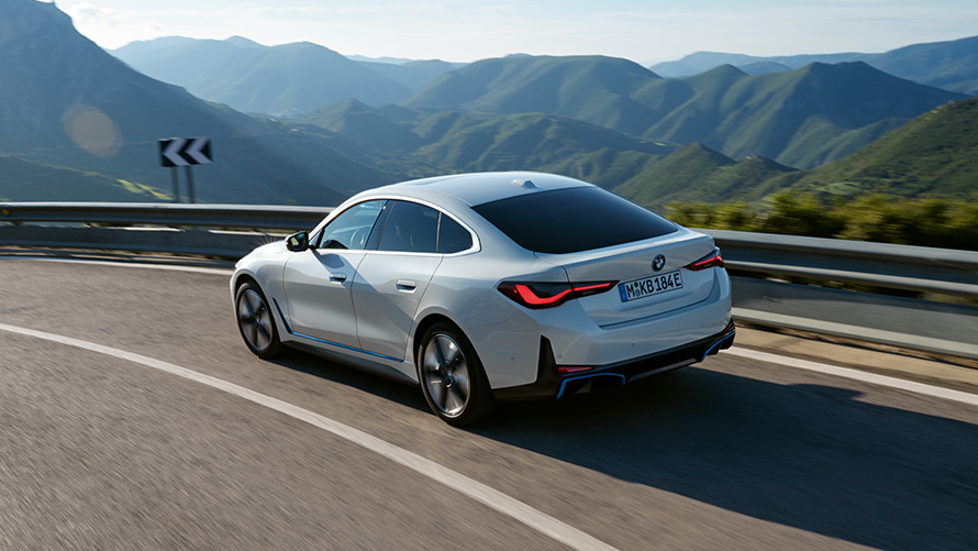 Tříčtvrteční pohled zezadu BMW i4 MeDrive40 G26 2021, jízdní BMW i4 eDrive40 G26 2021 Mineral White (bílá) tříčtvrteční jízdní záběr zezadu