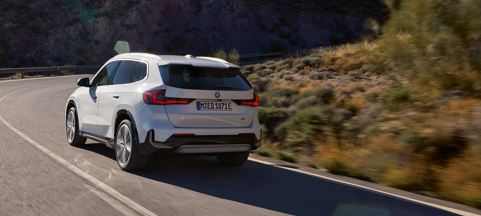 BMW iX1 U11 BEV video o jízdní dynamice BMW iX1 U11 BEV 2022 metalický lak Mineral White dvoutřetinový pohled zezadu jízdní záběr na horské silnici dynamické video