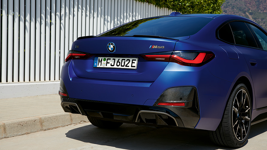 BMW i4 M50 G26 2021 metalick&yacute; lak Individual Frozen Portimao Blue (modr&aacute;) j&iacute;zdn&iacute; tř&iacute;čtvrtečn&iacute; pohled zezadu u b&iacute;l&eacute;ho plotu
