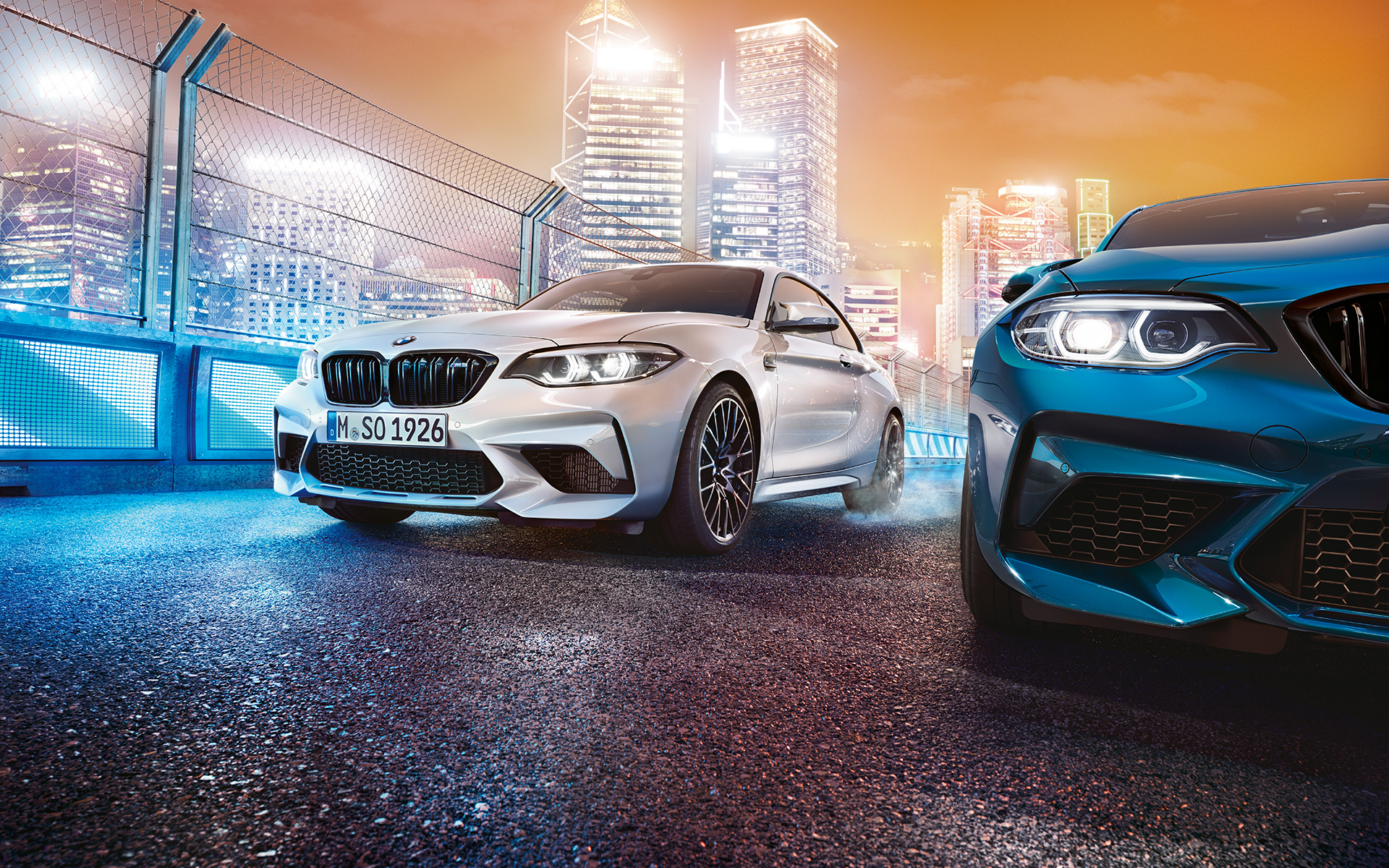 BMW M2 Competition z předního pohledu Tři BMW M2 Competition z předního pohledu s osvětleným městem v pozadí.