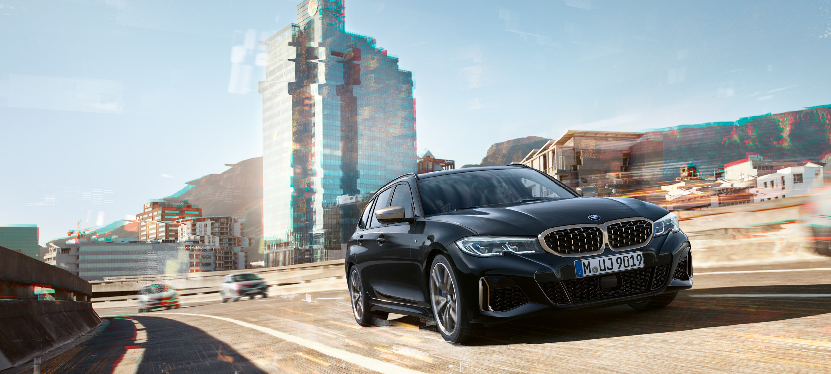 Jízdní tříčtvrteční záběr zepředu před městským prostředím BMW M340i xDrive Touring, Jízdní tříčtvrteční záběr zepředu před městským prostředím
