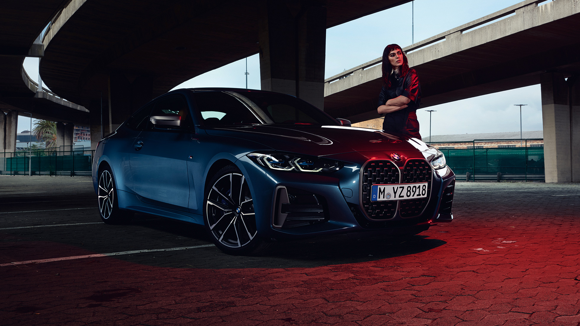 Model stojící vedle BMW M440i xDrive Coupé G22 2020 ze tříčtvrtečního pohledu z boku BMW M440i xDrive Coupé G22 2020 v metalické barvě Arctic Race Blue (modrá) ze tříčtvrtečního pohledu z boku s modelem