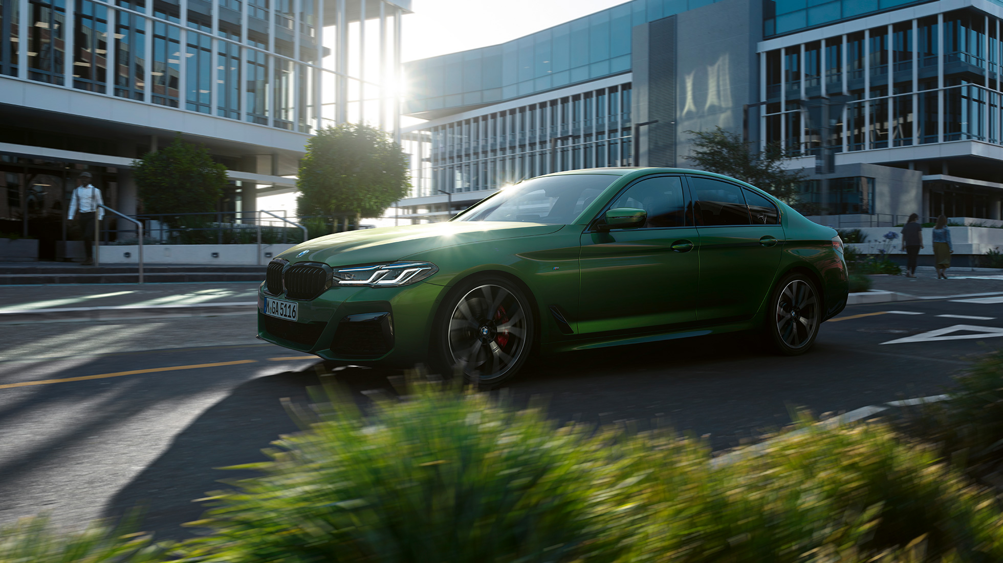 BMW M550i xDrive Sedan G30 LCI Facelift 2020 z bočního pohledu při jízdě BMW M550i xDrive Sedan G30 LCI Facelift 2020 v metalické barvě BMW Invidividual Verde Ermes (zelená) z bočního pohledu při jízdě centrem města